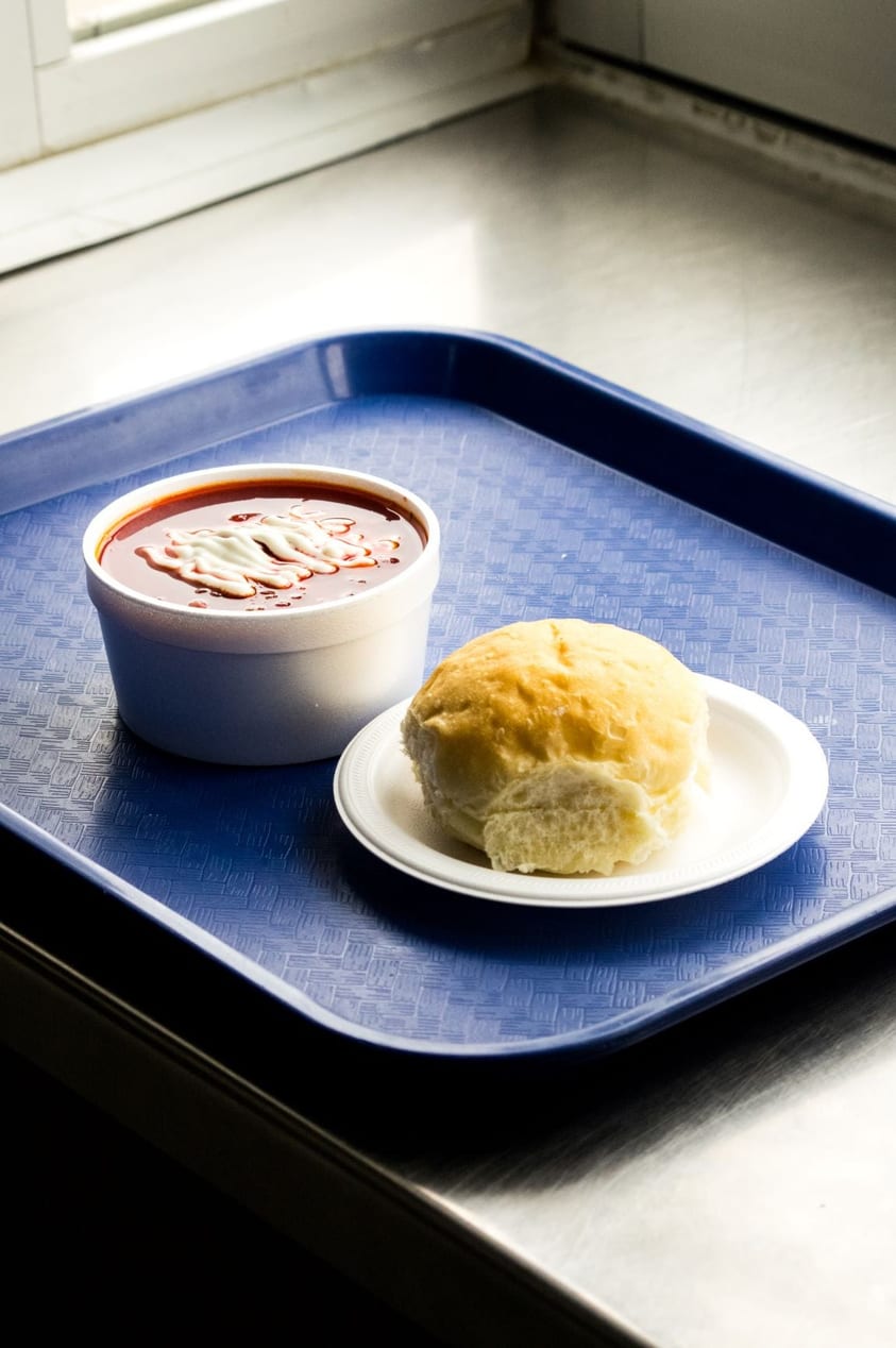 Borscht with sour cream and a dinner bun on a tray by the window