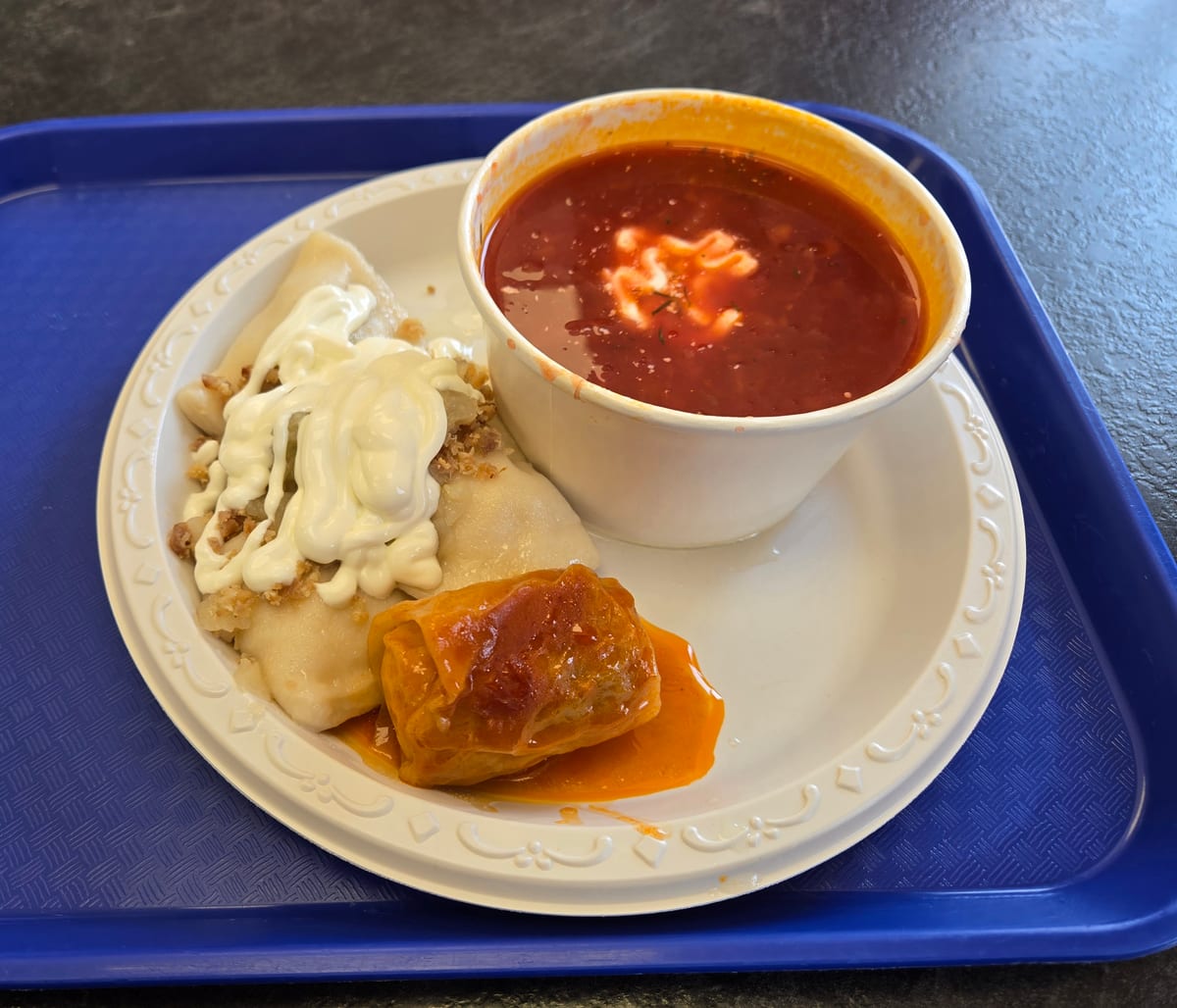 A bowl of borscht with sour cream beside perogies and a cabbage roll on a tray