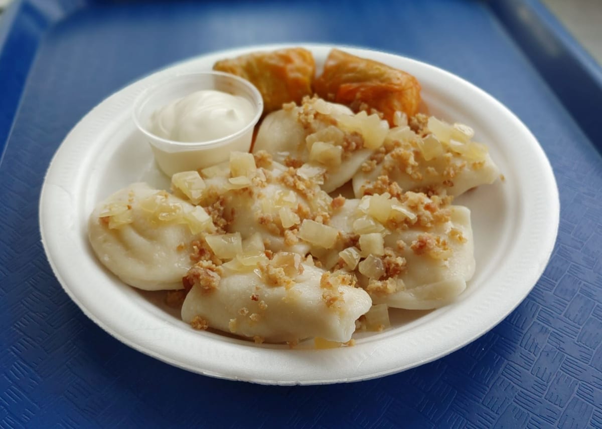 Perogies with onions and bacon bits, cabbage rolls and sour cream on a white plate