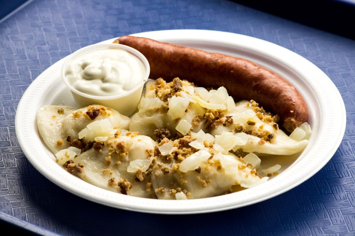 Perogies with fried onions and bacon bits, a farmer sausage and sour cream on a blue tray