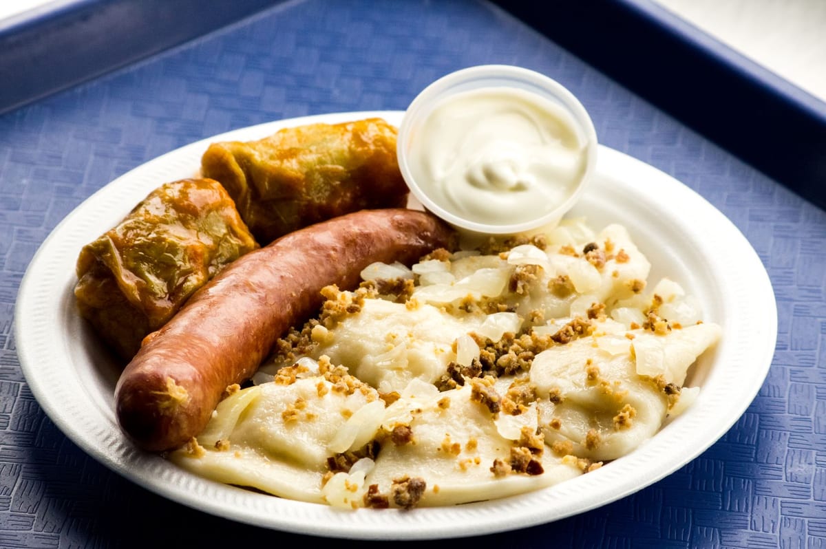 A Super Combo on a blue tray: perogies with bacon bits and onions, two cabbage rolls, a sausage and sour cream